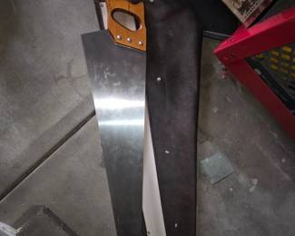 Large Hand Saw with Leather Scabbard — Long two-man style hand saw with a varnished hardwood pistol grip and full-length steel blade stored in a stitched leather (or leather-like) scabbard. The blade appears clean with fine crosscut teeth along one edge; handle secured with three visible bolts. Good solid condition with light surface marks on blade and scabbard shows minimal wear and intact snaps. Useful for timber framing, pruning large logs, or as a display tool; overall length about 48 inches.