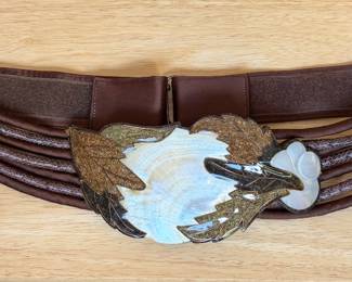 cinch belt featuring a decorative statement buckle with an iridescent mother-of-pearl center and leaf-shaped accents.