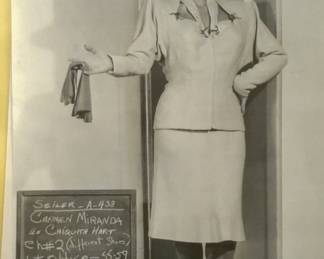 Black and white costume test photograph of a skirt suit and hat with a production slate visible