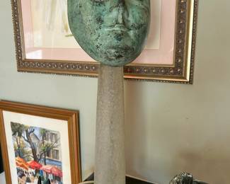Green patinated sculptural face displayed on a tall column with a round base from the Tom Culver estate