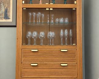 Rounded rattan-style display and bar cabinet with glass-front upper storage, glass shelves, lower drawers and brass-tone hardware. Its curved silhouette makes a statement for a vintage interior. Glassware and decorative pieces shown are separate sale items; inquire at the sale for individual availability.
