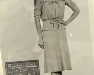 Black and white costume test photograph showing a belted dress and cardigan with a production slate