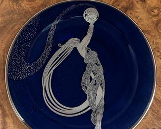 Deep blue decorative plate with a silver tone fashion figure and flowing ribbon motif