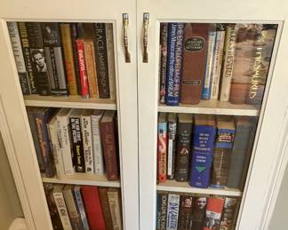 Estate library with books on film fashion entertainment and reference subjects in a white glass front cabinet