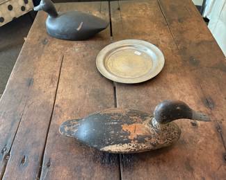 An early tavern table with stretcher base. Decoys are unknown makers. The forward one could be a Stevens the other is a hollow black duck decoy. Pewter plate.