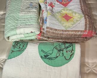 Vintage Quilt Lot with Appliqué Child's Quilt A stacked lot of vintage quilts including a hand-appliquéd child's quilt with green circular medallions featuring figural designs on a white ground, alongside a folded patchwork quilt with brown sashing and a green-bound quilt beneath. The visible hand quilting is even and the appliqué work is intact where shown. Condition across the full stack was not individually assessed. A nice grouping for quilt collectors and nursery decor buyers.