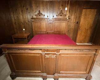 Antique Carved Bed with Matching Nightstand - An antique bed with an elaborately carved headboard and footboard, featuring raised panels, fluted columns, applied foliate carving, and turned finials at the crest. The footboard carries matching carved detail and rests on turned bun feet. A matching nightstand with a lower shelf is included. The finish is warm and even with age-appropriate wear; mattress and bedding are not included, and frame rails and completeness should be confirmed in person. A commanding antique bedroom set piece for buyers furnishing a period room.