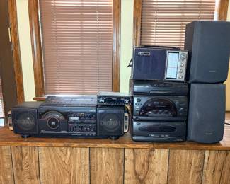 Vintage Stereo Equipment Lot - A vintage audio lot including a Soundesign dual-cassette boombox with CD player and graphic equalizer, a Sharp 3-disc rotary changer component system with dual cassette deck, a pair of Sharp speakers, a Pioneer car stereo head unit, and a Baylor FM/AM 14-transistor portable radio. The pieces show light dust and surface wear; the Baylor radio in particular has appealing vintage styling with its leather carry handle. Working condition not confirmed on all units — sold as found. A good lot for vintage stereo enthusiasts and boombox collectors.