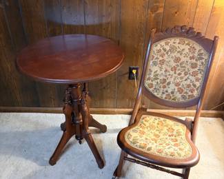 Victorian Oval Parlor Table and Folding Tapestry Chair - A two-piece lot pairing an antique oval parlor table on a turned and pierced pedestal base with splayed legs, and an antique folding chair with floral tapestry upholstery on the seat and back. The table top shows light surface marks and a visible seam across the center; the chair has a carved crest rail and appears structurally sound with the tapestry intact. Both pieces show honest age wear consistent with use. A good entry-level antique furniture lot for a sunroom, entry, or bedroom corner.