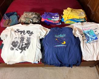 Vintage T-Shirt and Clothing Lot - A large vintage clothing lot including a Sugar Ray band t-shirt, a StarDate shirt from the University of Texas at Austin McDonald Observatory, and a 15th Annual Destin Shark Tournament tee from Destin, Florida. Also included are stacks of colored graphic tees, camouflage hunting pants and jackets, and several color-block hoodies. The shirts show general wash wear and softening; individual sizes and condition were not inventoried. A strong lot for vintage clothing resellers — the band tee, observatory shirt, and tournament tee each pull a different collector.