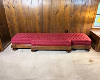 Victorian Hall Bench A long Victorian hall bench with a deep button-tufted top in red upholstery, set on a wood base with paneled sides and turned bun feet. The tufting runs the full length in an even diamond pattern and the upholstery is full throughout. The wood base carries a warm finish with molded trim along the top and bottom edges. An unusually long bench with real presence in an entry or hallway.