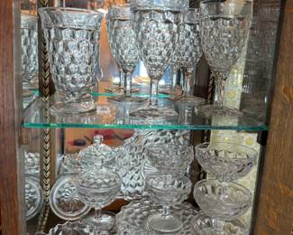 Cut Glass Cube Pattern Glassware Collection A collection of pressed glass in a cube pattern, including water goblets, a tall footed vase, footed compotes, lidded candy dishes, and small stemmed dessert bowls. The glass is clear and bright with strong pattern definition across the cube facets. Displayed across two shelves of a mirrored cabinet. A cohesive grouping in a single recognizable pattern.