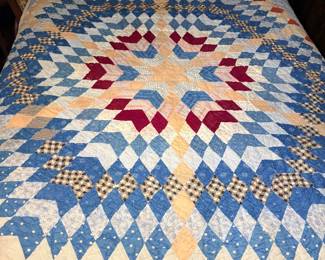 Antique Lone Star Patchwork Quilt - A hand-pieced antique quilt in the Lone Star pattern, radiating from a central eight-point star in blue, red, burgundy, tan, and white printed cottons, including indigo calicos, polka dots, and small-scale checks. The hand quilting is dense and even throughout and the piecing is tight. Condition is honest for its age — the binding shows fraying and several worn patches along the lower edge, and a few fabrics show age toning. A genuine handmade quilt for collectors of antique textiles and Lone Star patterns.