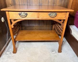 Antique Oak Library Table with Lattice Sides - An antique oak library table with a single long drawer, ornate pierced brass pulls in an Art Nouveau style, and distinctive lattice-work panels on both sides above a full lower shelf. The quartersawn grain shows clearly across the top and shelf, and the finish is bright and even with only minor wear. The lower shelf and legs appear solid with no visible damage. An attractive antique oak table for a hallway, entry, or behind a sofa, and the lattice detailing sets it apart from ordinary library tables.