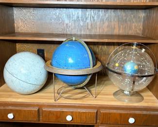 Three Vintage Celestial Globes - A three-piece lot of celestial and astronomical globes: a moon globe mapping the lunar seas and craters, a blue constellation globe mounted in a wire stand with a calendar meridian ring, and a clear acrylic planetarium-style globe with an Earth sphere suspended inside a star field. All three show light surface wear and dust; the constellation globe's stand shows some oxidation. Celestial globes are popular with both astronomy collectors and mid-century decor buyers, and a matched group of three is an uncommon find.