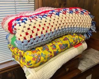 Afghan and Quilt Lot A stacked lot including a hand-crocheted afghan in red, white, and blue with a fringed edge, a blue and cream crocheted throw, a yellow quilt with a printed owl pattern, and a cream quilt at the bottom. The crochet work is even and the pieces are clean in the photo. Full condition of each was not assessed folded.