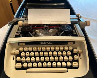 Royal Portable Typewriter with Case A Royal portable typewriter in a cream and black body with round cream keys, shown seated in its hard carrying case with a sheet of paper loaded in the platen. The keys, ribbon spools, and carriage return lever are all present, and the body shows light age yellowing typical of the period. Working condition not confirmed — the key action, ribbon, and carriage were not tested, sold as found. A handsome vintage manual typewriter for writers, decorators, and typewriter collectors.