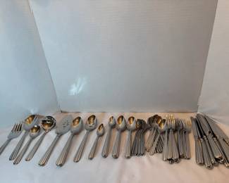 Stainless Flatware Service A stainless flatware service in a slender ribbed handle pattern, including dinner forks, salad forks, teaspoons, soup spoons, serving spoons, a slotted server, and knives. Several serving pieces carry gold-toned bowls. The set is bright with a clean satin and polished finish. A large, usable everyday service.