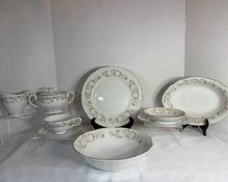 China Service with Silver Floral Swag Border A china service in white with a delicate gray and silver floral swag border and platinum rim trim. The set includes dinner plates, salad plates, saucers, teacups, a covered sugar bowl, a creamer, a gravy boat with underplate, an oval serving platter, and a round vegetable bowl. The platinum banding is bright and the pattern is crisp across the pieces. An elegant service with a clean, formal look.