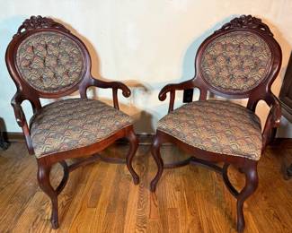Pair of Victorian Balloon Back Parlor Chairs Two matching parlor chairs with carved floral crests, oval upholstered backs, and open scrolled arms on cabriole front legs. The upholstery is a paisley pattern in gold, burgundy, and teal on both the seats and backs. The wood carries a rich reddish finish with the carving crisp at the crest. A handsome matched pair for a formal sitting room.