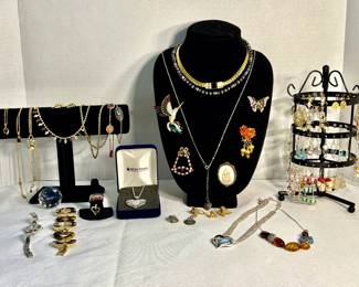 Costume Jewelry Lot A costume jewelry lot displayed across a bracelet bar, necklace bust, earring tree, and a gift box. Included are a rhinestone collar necklace, a butterfly brooch, a cameo-style brooch, a bird brooch, beaded and chain necklaces, bangles, rings, and a quantity of pierced earrings. Metal content and stones have not been tested. Pieces show varying degrees of age and wear.