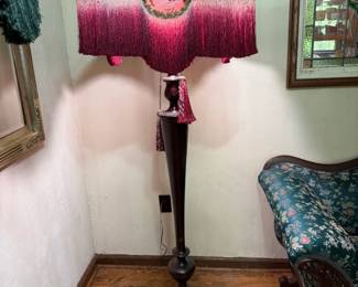 Floor Lamp with Pink Beaded Fringe Shade A floor lamp on a tall dark wood column with a wide shade in pink and red, trimmed in long beaded fringe with a decorative center medallion and hanging tassels. The fringe is full and the shade holds its shape. Working condition not confirmed — the lamp was not tested. Sold as found.
