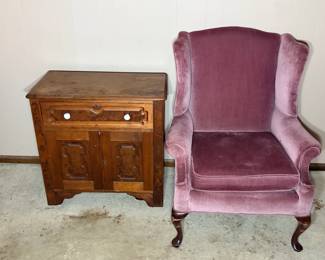 Wingback Chair and Carved Wood Cabinet A two-piece lot pairing a mauve velvet wingback chair on cabriole front legs with a small carved wood cabinet. The cabinet has a single top drawer with a turned knob over two doors with raised carved panels, finished with a shaped apron and bracket feet. The chair's velvet is full and even across the seat and back, and the cabinet carries a warm wood finish. A practical pairing for a bedroom or reading corner.