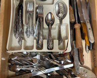 Large Flatware Lot with Ornate Silverplate Pattern A full kitchen drawer of flatware including a set in an ornate scrolled pattern — forks, spoons, serving spoons, and slotted servers — displayed in a tray, plus a deep layer of additional mixed flatware beneath. A second group of wood-handled carving knives and steak knives is included, along with a Kitchen Magic slicer. Individual pieces were not sorted, counted, or inspected for hallmarks in the photo. The maker's marks and metal content on all pieces should be verified before listing.
