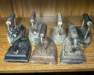Seven Antique Sad Irons A lot of seven antique cast iron sad irons with looped handles and pointed noses, in varying sizes and surface conditions. Several retain a darker original surface while others show orange oxidation and pitting consistent with age and storage. These were used as flatirons and are sold as decorative — no restoration or cleaning has been done. Antique sad irons are steady sellers as bookends, doorstops, and farmhouse kitchen decor, and a group of seven allows a buyer to display them as a set.