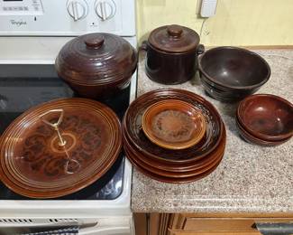 Brown Glazed Stoneware Set A brown glazed stoneware grouping including two lidded bean pots, a handled bowl, dinner plates, smaller plates, and nesting bowls. Several pieces carry a darker decorative pattern on a lighter ground. The glaze is glossy throughout with no chips visible in the photo. A usable set with the kind of finish that reads well in a farmhouse kitchen.
