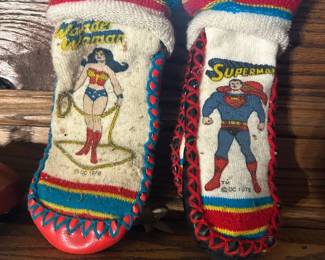 Vintage 1978 DC Comics Wonder Woman and Superman Moccasins A pair of children's moccasin-style slippers with screen-printed Wonder Woman and Superman character art, finished with red whipstitch lacing and red soles. The DC Comics copyright and 1978 date are visible printed on the fronts. Both show soiling, print wear, and general use consistent with age. Licensed 1970s DC merchandise has a real collector following, and dated original character items like these are getting scarce.