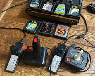 Atari 2600 Console Lot with Games and Controllers An Atari 2600 lot including the console, two joystick controllers, and a carrying case of game cartridges. Legible titles include Pac-Man, Vanguard, Space Invaders, and Maze Craze, with several additional cartridges in the case rack that were not fully readable in the photo. The console and controllers show light surface wear; cartridge labels vary in condition. Working condition not confirmed — nothing was tested, sold as found. A strong retro gaming lot, and the cartridge titles should be fully inventoried since individual games vary widely in value.