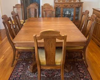 Oak dining table with 12 chairs and five 12 inch leaves above a hand knotted rug made in Iran