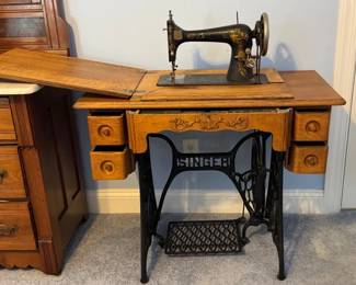 Singer treadle sewing machine housed in a carved wooden cabinet with side drawers and a cast iron base