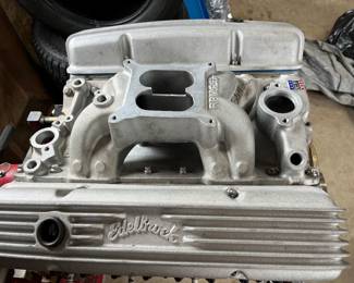 V8 small-block engine on an engine stand, featuring finned Edelbrock aluminum valve covers and a gold-painted oil pan.