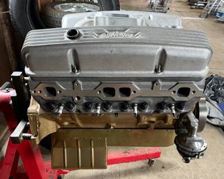 V8 small-block engine on an engine stand, featuring finned Edelbrock aluminum valve covers and a gold-painted oil pan.