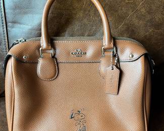 Saddle brown Coach x Peanuts Snoopy Mini Bennett Satchel featuring an embossed graphic of Snoopy on the front.