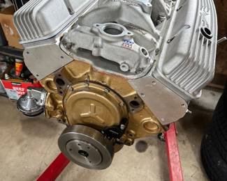 V8 small-block engine on an engine stand, featuring finned Edelbrock aluminum valve covers and a gold-painted oil pan.
