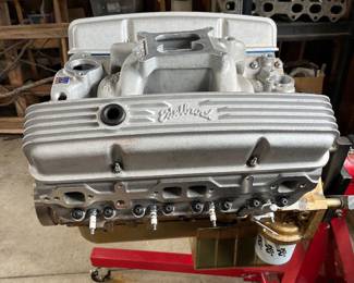 V8 small-block engine on an engine stand, featuring finned Edelbrock aluminum valve covers and a gold-painted oil pan.