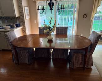 Oak kitchen table with leaves and 4 covered cloth chairs, vase of flowers decoration