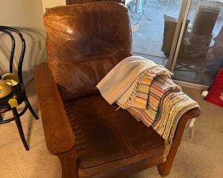 Mission-style leather and oak armchair featuring warm, worn brown upholstery and wide wooden armrests, striped woven throw blankets