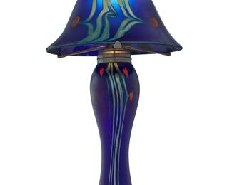 2226 Carl Radke (b. 1950) A Favrile style glass table lamp, late 20th century With pulled feather design, issuing three arms and a single light, electrified Appears unmarked Height overall 16 7/8 in., diameter 8 7/8 in.; height of shade 6 in. Estimate: $400 - $600