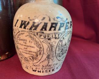 handled jugs including a 9-inch tan jug with heart and feather motif, a brown 8.5-inch jug, a large 10-inch speckled brown jug, and an I.W. Harper Kentucky Whiskey ceramic advertising jug.