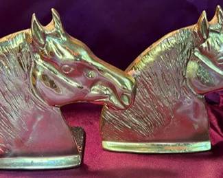 Decorative brass items including a pair of turned candlesticks, Royal Coat of Arms wall plaque, horse head bookends, and a leaf-form dish. All pieces are crafted from brass with detailed designs. 
