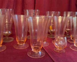 Assorted pink Depression glass stemware pieces, including footed glasses, a coupe, and a small cordial. The glass has a soft pink hue typical of Depression-era glassware.