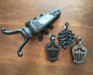 Cast iron cricket and three decorative cast iron trivets, each with ornate lattice or lyre designs.