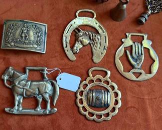 1959 India-marked etched brass bowl, decorative brass harness ornaments with horse, hand, and barrel motifs, a commemorative belt buckle, brass bells, and a metal key chain with a tree motif.