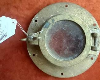 Brass and glass lantern with carrying handle, a small brass porthole with glass window and mounting holes, a brass chamberstick, and two brass candleholders. All items are brass, suitable for maritime or decorative use.