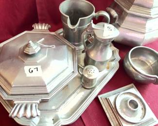 International Silver Co. pewter tea set, including teapot, sugar bowl, creamer, lidded sugar, mug, salt shaker, two octagonal trays, ladle, and a sauce dish. Each piece is marked on the base. Moderate wear and tarnish consistent with use.