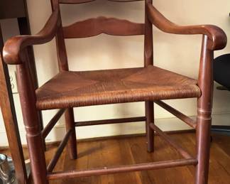 Wooden armchair featuring a rush-woven seat and gently curved arms. The chair has turned legs with supportive stretcher bars and a decorative crest rail.